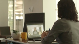 Woman sitting at a desk watching a virtual meeting on her laptop