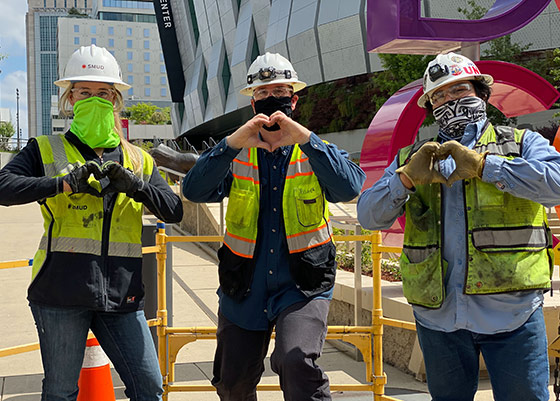 SMUD employees with hardhats and face masks in downtown Sacramento making heart shapes with their hands