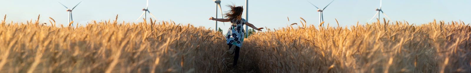 Young girl running through a field with wind turbines in the background.