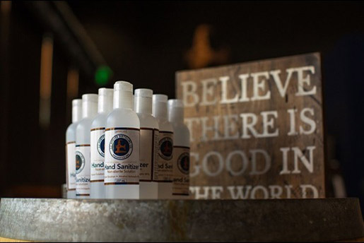 Bottles of sanitizer in front a sign that says "Believe there is good in the world."